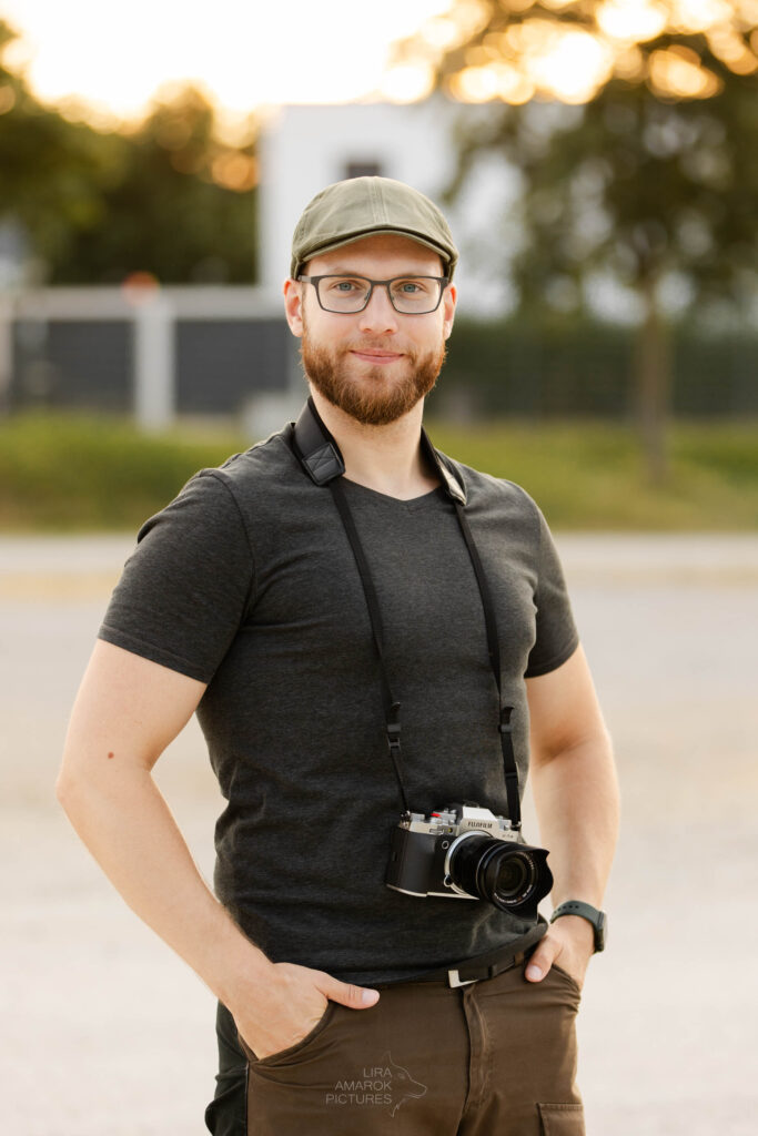 Bild eines stehenden Mannes mit Kamera, der in die Kamera schaut