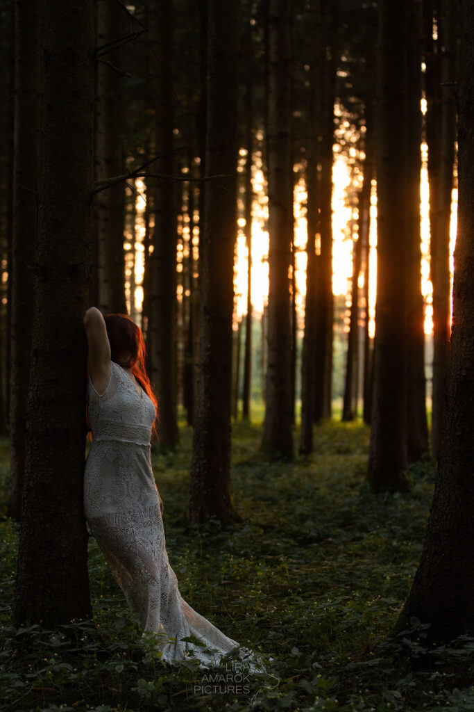 Frau mit weißem Kleid steht bei Sonnenuntergang im Wald
